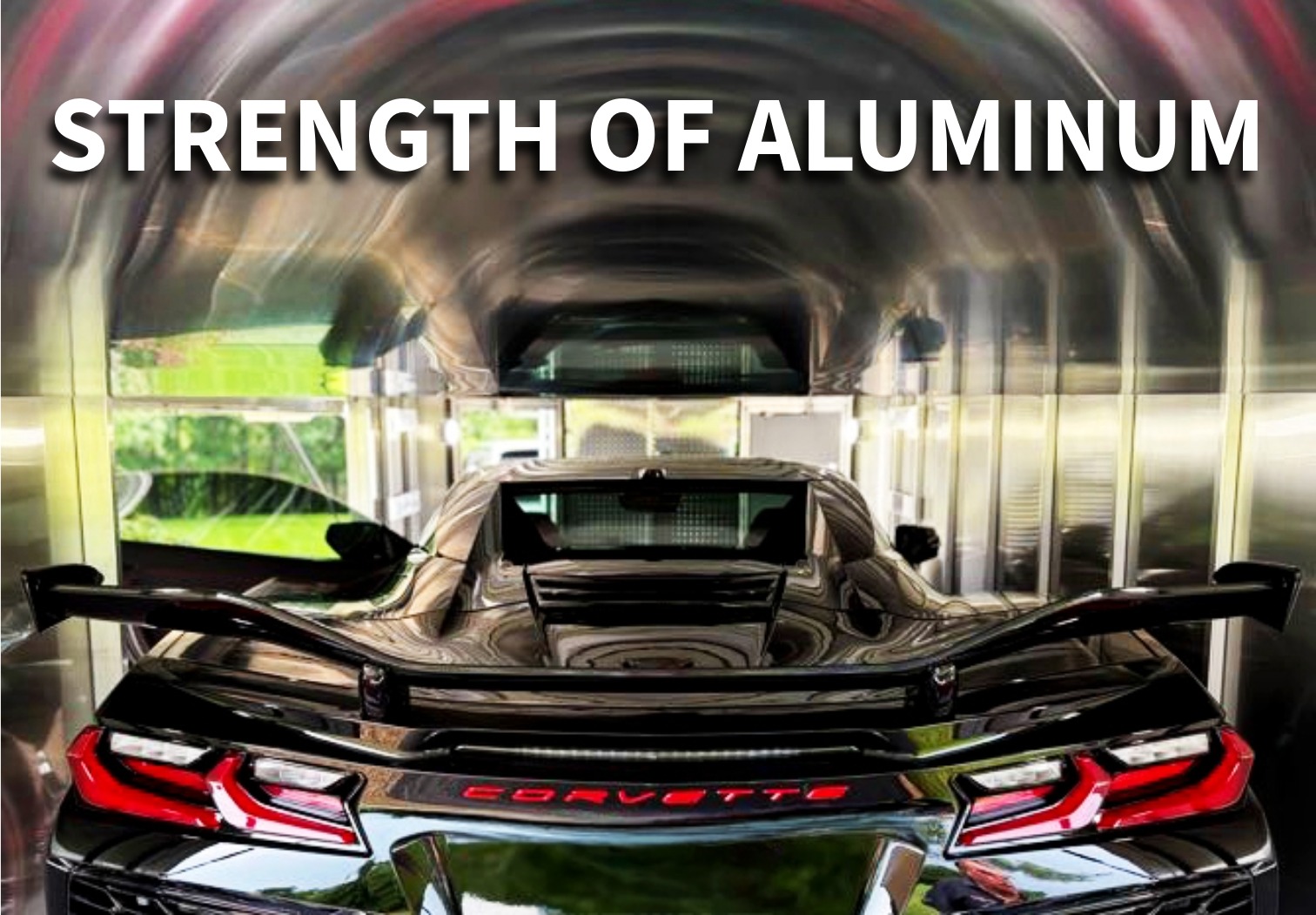 trailex-aluminum-trailers-strength-of-aluminum Interior back image of an aluminum enclosed car trailer. A black corvette is shown parked inside the trailer, and the back end of the vehicle is centered in the image. Across the top in bold white letters, it reads “Strength of Aluminum”.